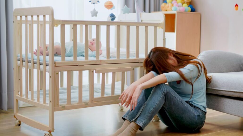 woman with postpartum depression next to crib